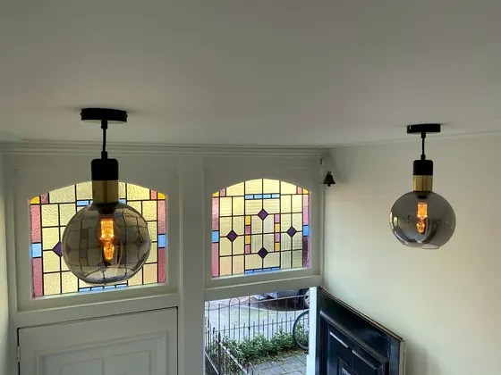 Twee hanglampen met amberkleurige bollen in een hal met glas-in-loodramen